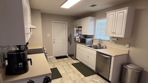 A modern kitchen with white cabinets, a black coffee maker, and a stainless steel trash can. - Charming 3BR 2BA 20 min drive to the Masters (Grovetown)