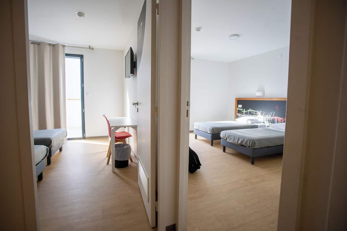 A hotel room with two beds, a desk, a chair, and a small trash bin.