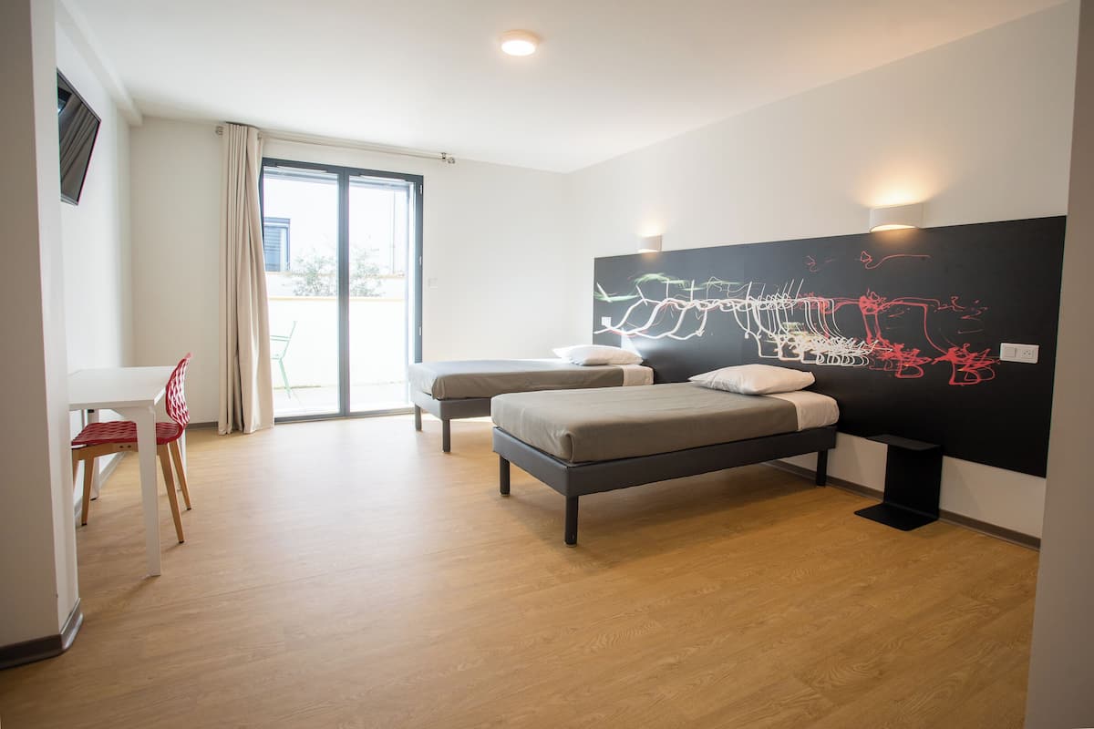 A modern bedroom with two beds, a large abstract painting, and a sliding glass door to the outside.