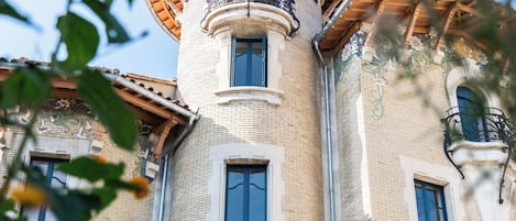 A building with a round tower, multiple windows, and a balcony with ornate railings.
