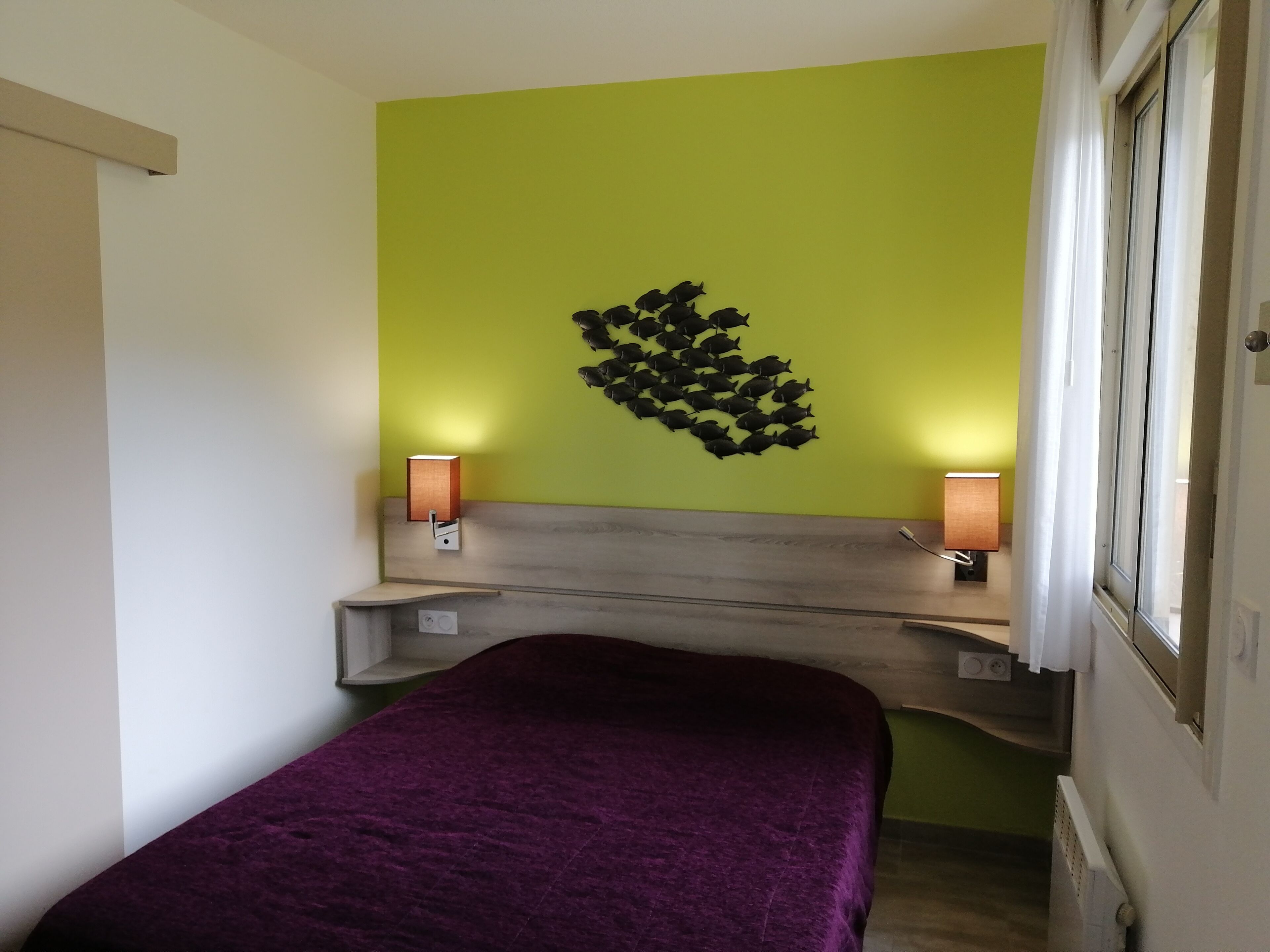 Une pièce avec un lit, un luminaire fixé au mur et une fenêtre.