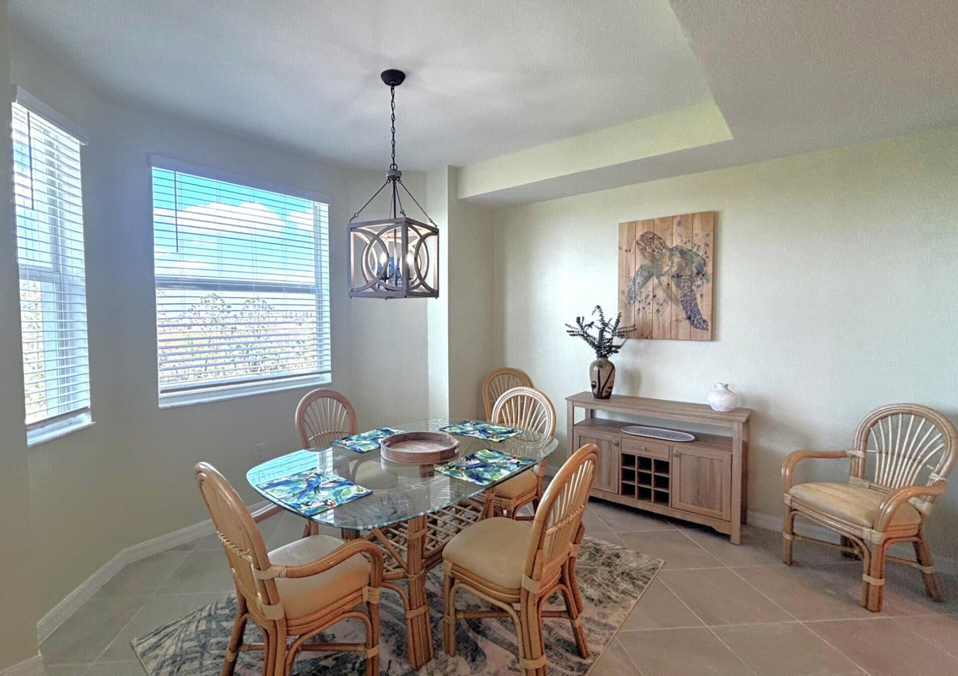 A dining area with a glass table, wicker chairs, a wooden cabinet, and a ceiling light fixture.