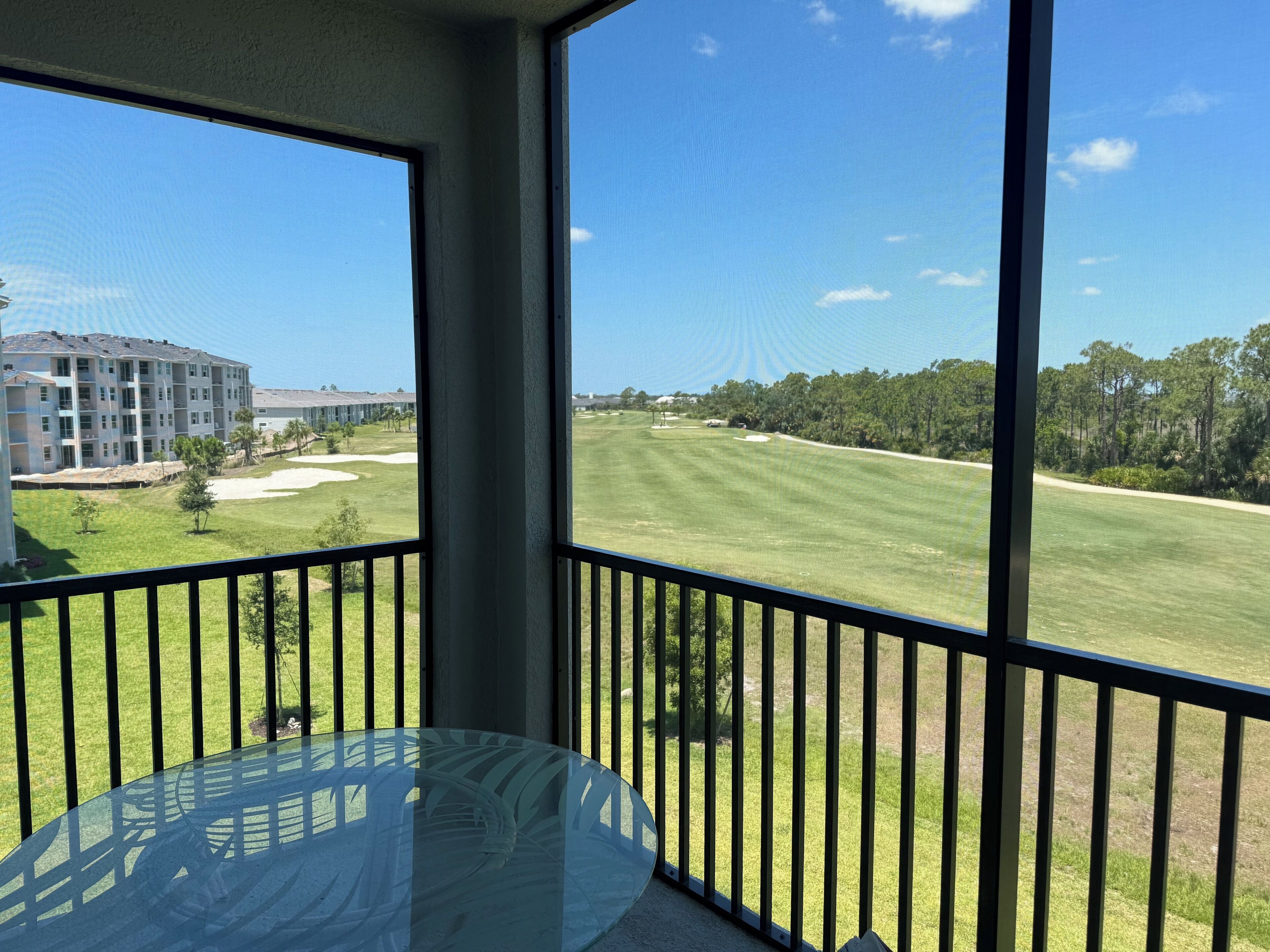 A balcony with a glass table and a view of a golf course and residential buildings.