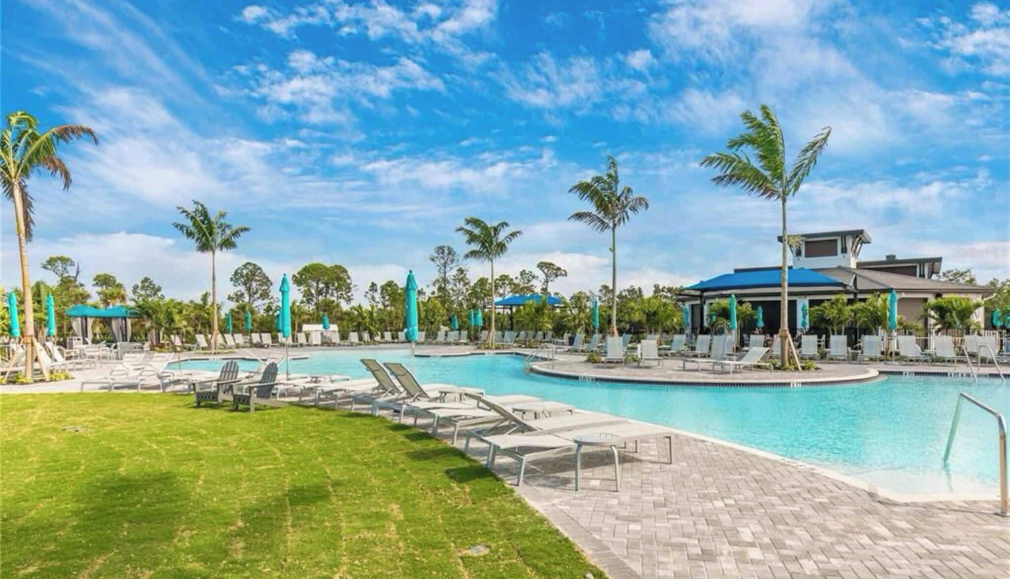 Ein Poolbereich einer Ferienanlage mit Liegestühlen und Sonnenschirmen, umgeben von Palmen und wolkenlosem Himmel.