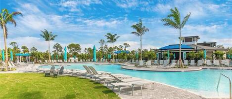 A resort pool area with lounge chairs and umbrellas, surrounded by palm trees and a clear sky.