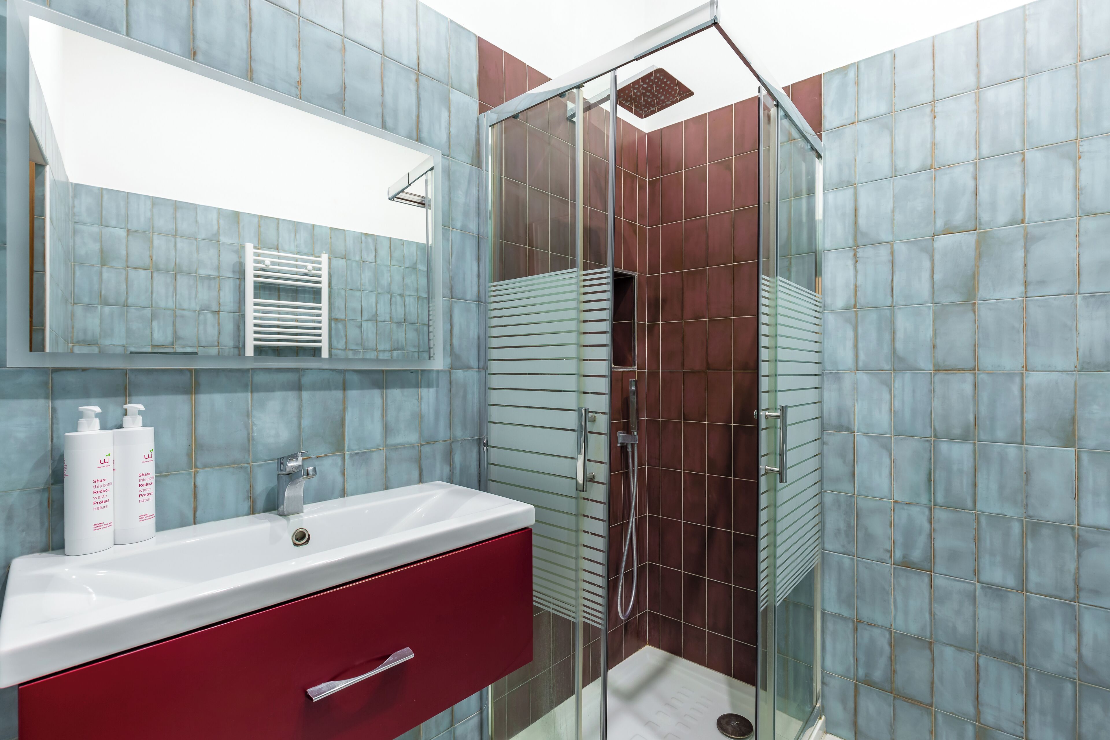 A modern bathroom with a glass shower enclosure, a white sink with a red cabinet, and a large mirror above the sink.