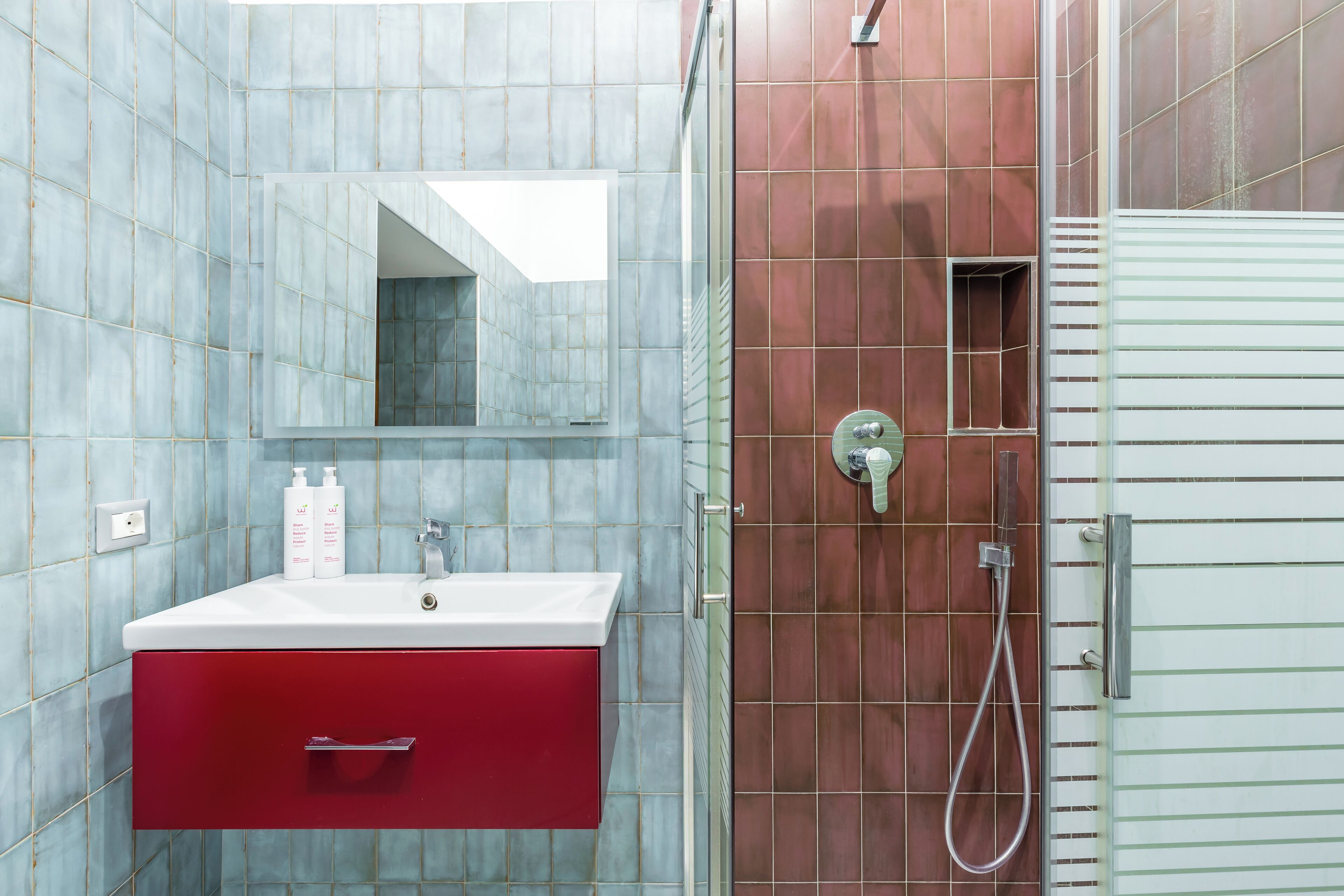 A bathroom with a white sink, red cabinet, and a shower area with a glass door.