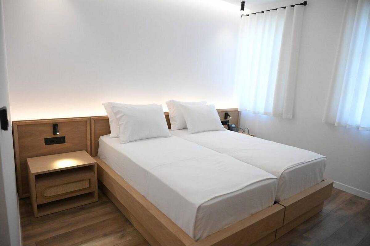 Un lit double avec une literie blanche, une table de chevet en bois et une petite table d’appoint.