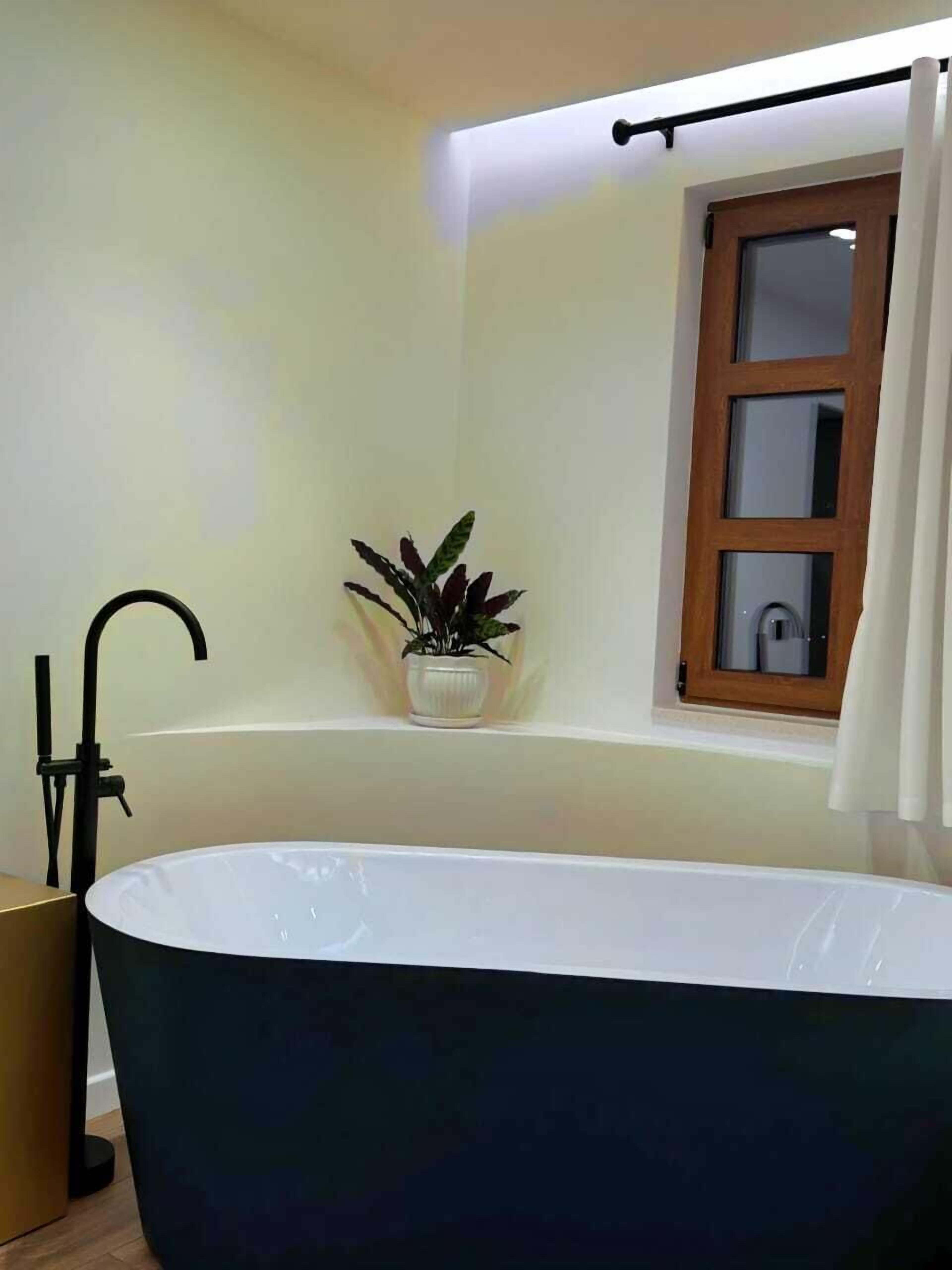 Une salle de bain moderne avec une baignoire sur pieds, une plante en pot posée sur une étagère et une fenêtre avec des rideaux.