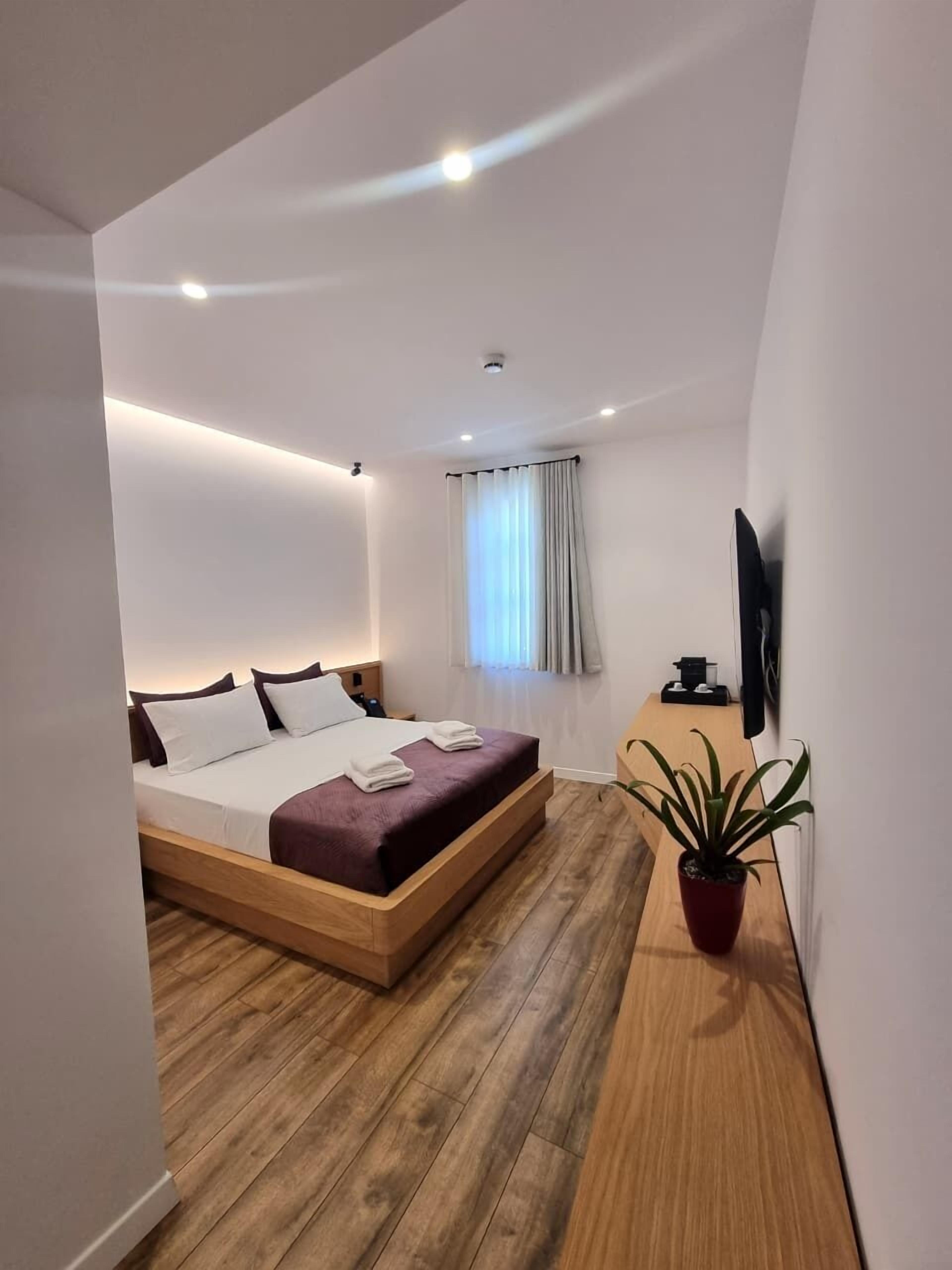 Ein modernes Schlafzimmer mit einem hölzernen Bett, einem kleinen Nachttisch, einem Fernseher und einer Topfpflanze.