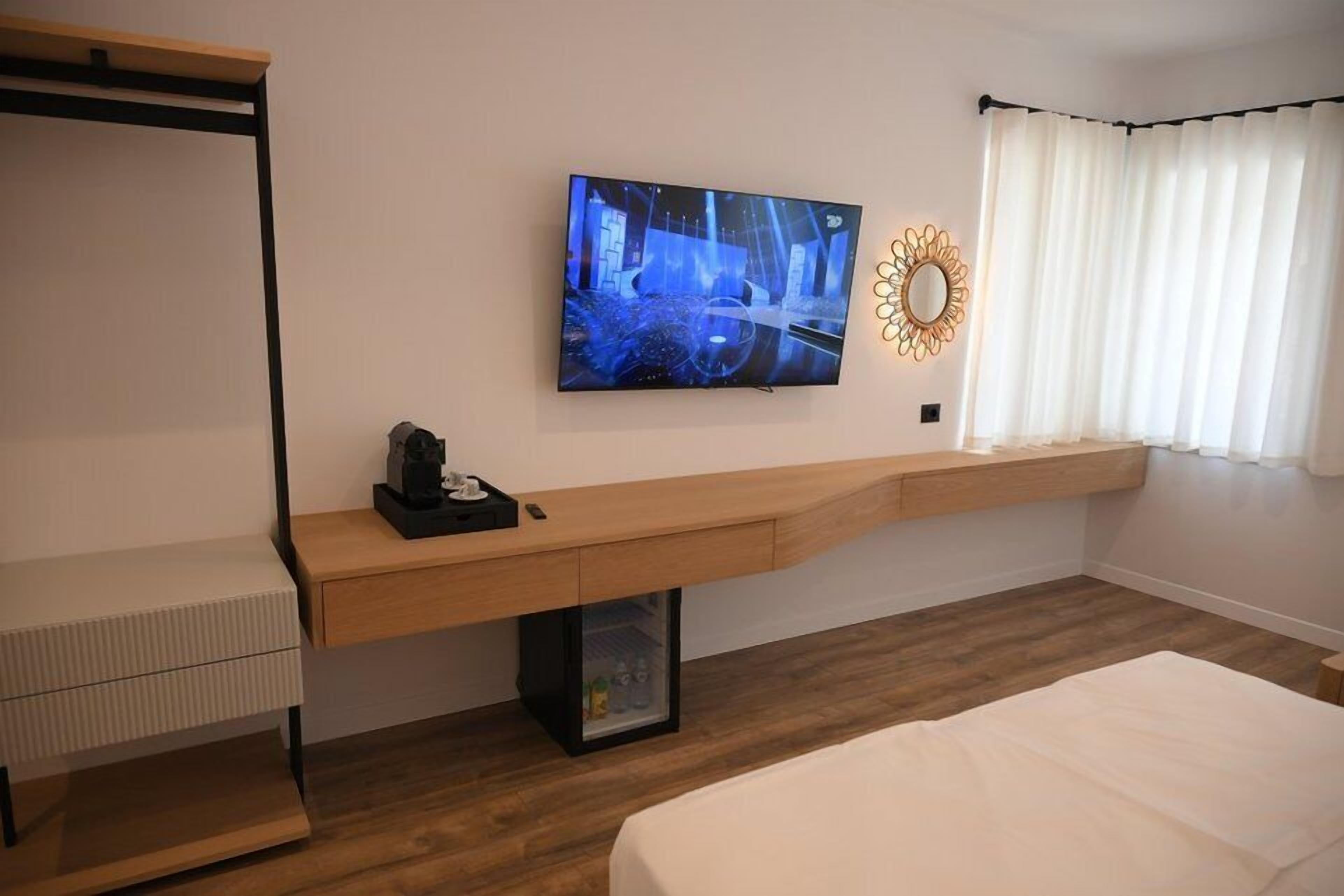 A modern hotel room with a bed, a desk with a computer, a TV, and a window with curtains.