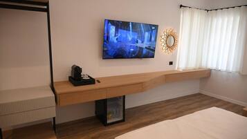 A modern hotel room with a bed, a desk with a computer, a TV, and a window with curtains.