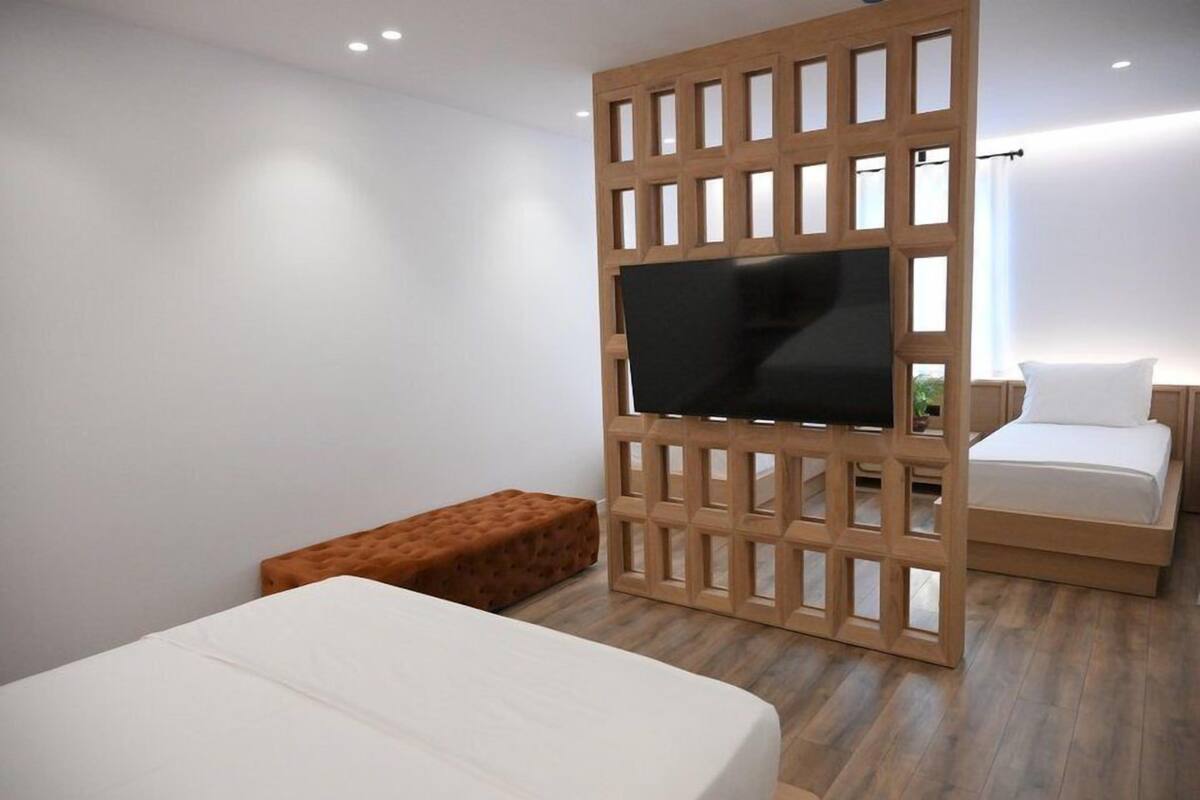Une chambre moderne avec une cloison en bois, un téléviseur à écran plat, un lit, un banc et une petite table de chevet.