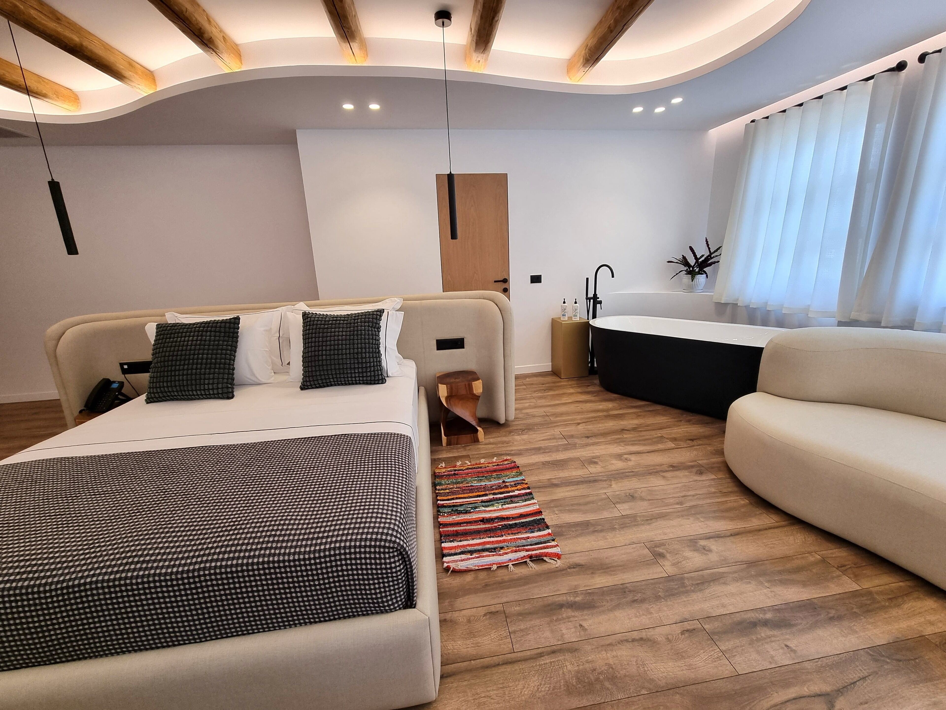 Una habitación de hotel moderna con cama, sofá, baño y suelo de madera.