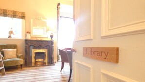 Une pièce chaleureuse avec une cheminée, un fauteuil vert et une pancarte « Bibliothèque » accrochée au mur.