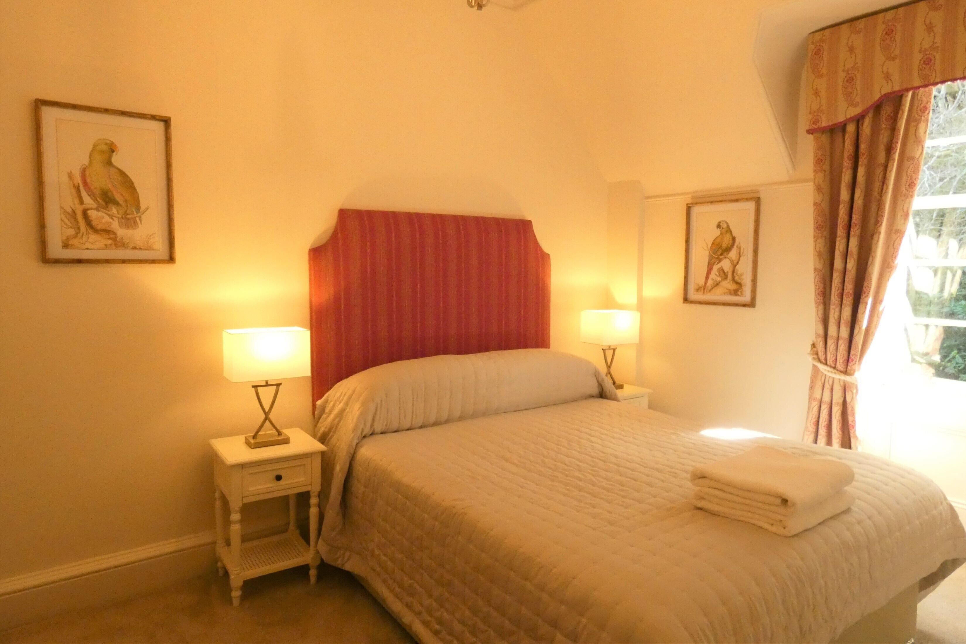 A bedroom with a bed, two bedside lamps, a nightstand, and two framed pictures on the walls.