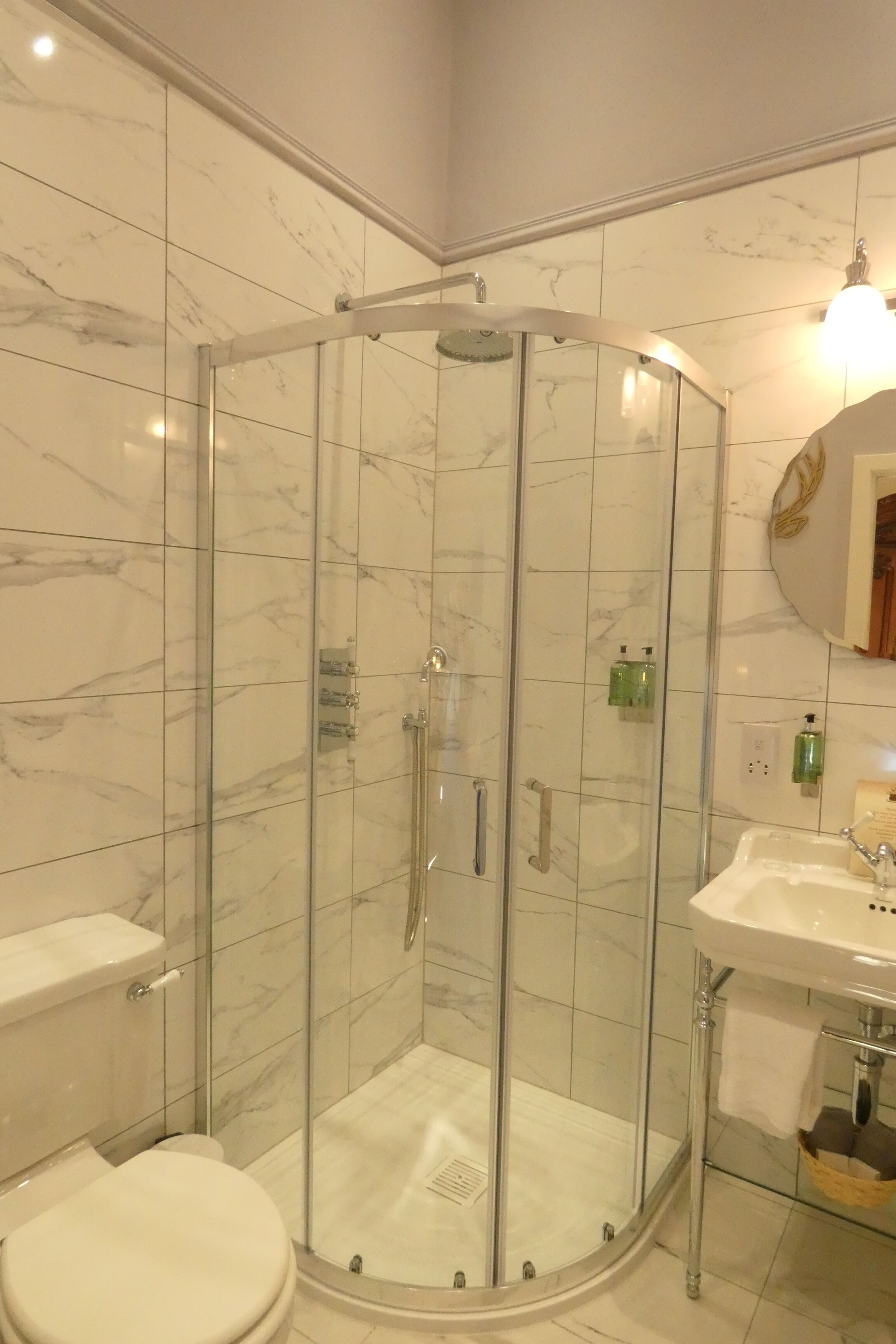 A modern bathroom with a glass-enclosed shower, a white toilet, and a sink with a mirror above it.