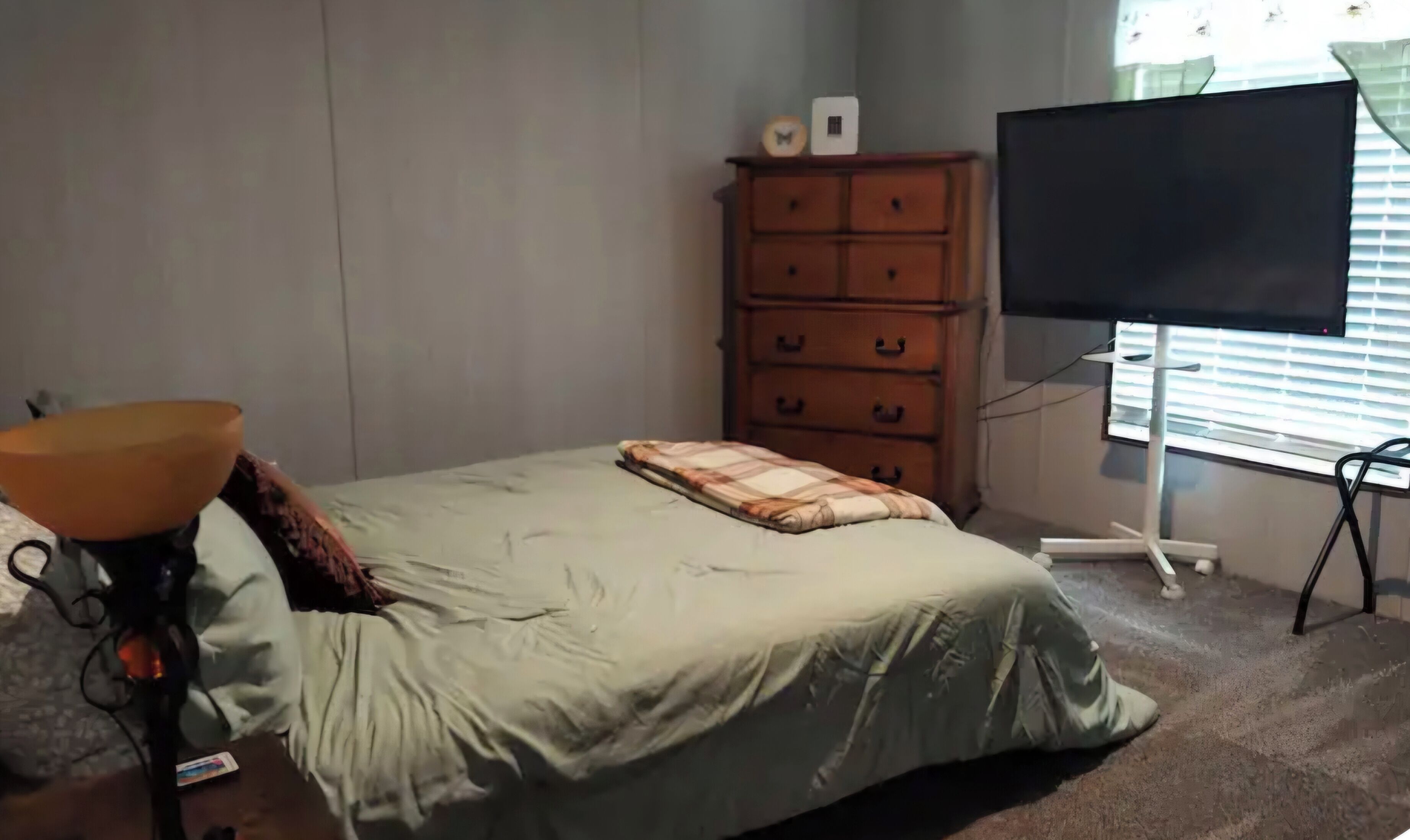 Un dormitorio con cama, cómoda, televisor y lámpara.
