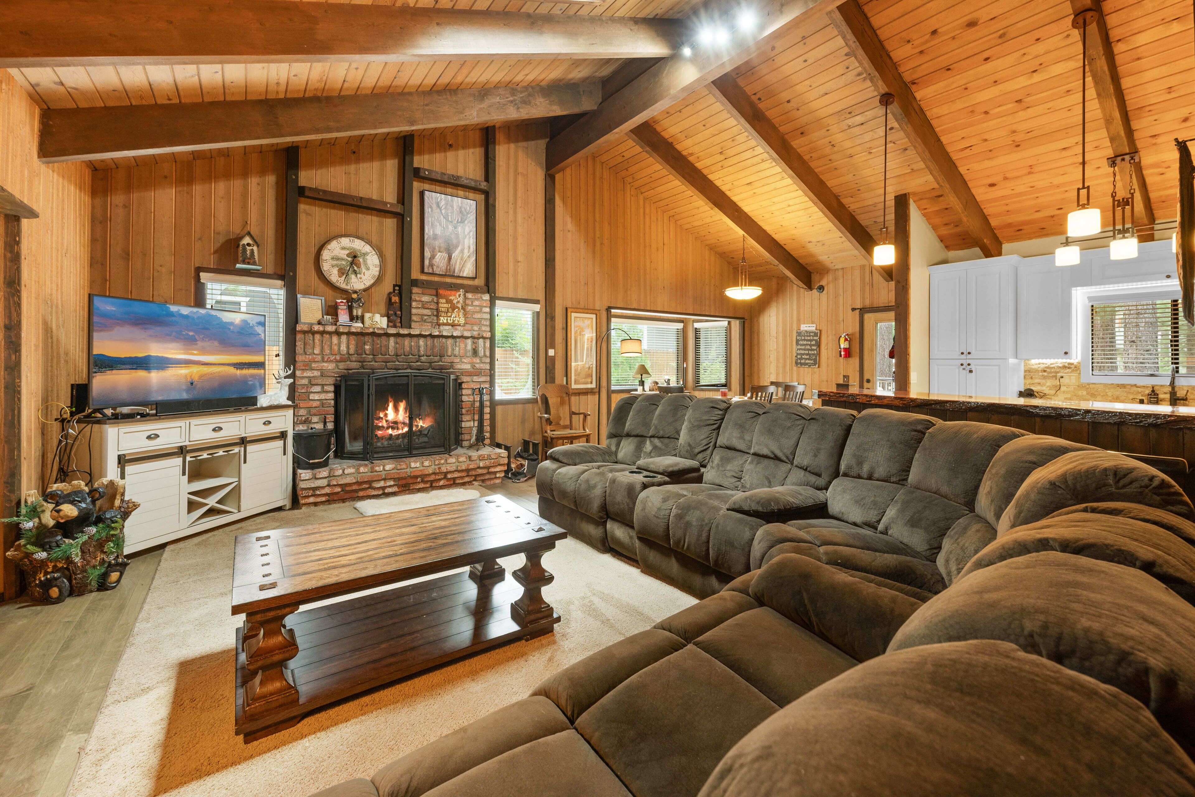 A cozy living room with a fireplace, wooden beams, a large sectional sofa, and a television.