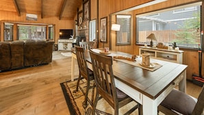 Interior acolhedor de uma cabana, com mesa de jantar de madeira, cadeiras e lareira.
