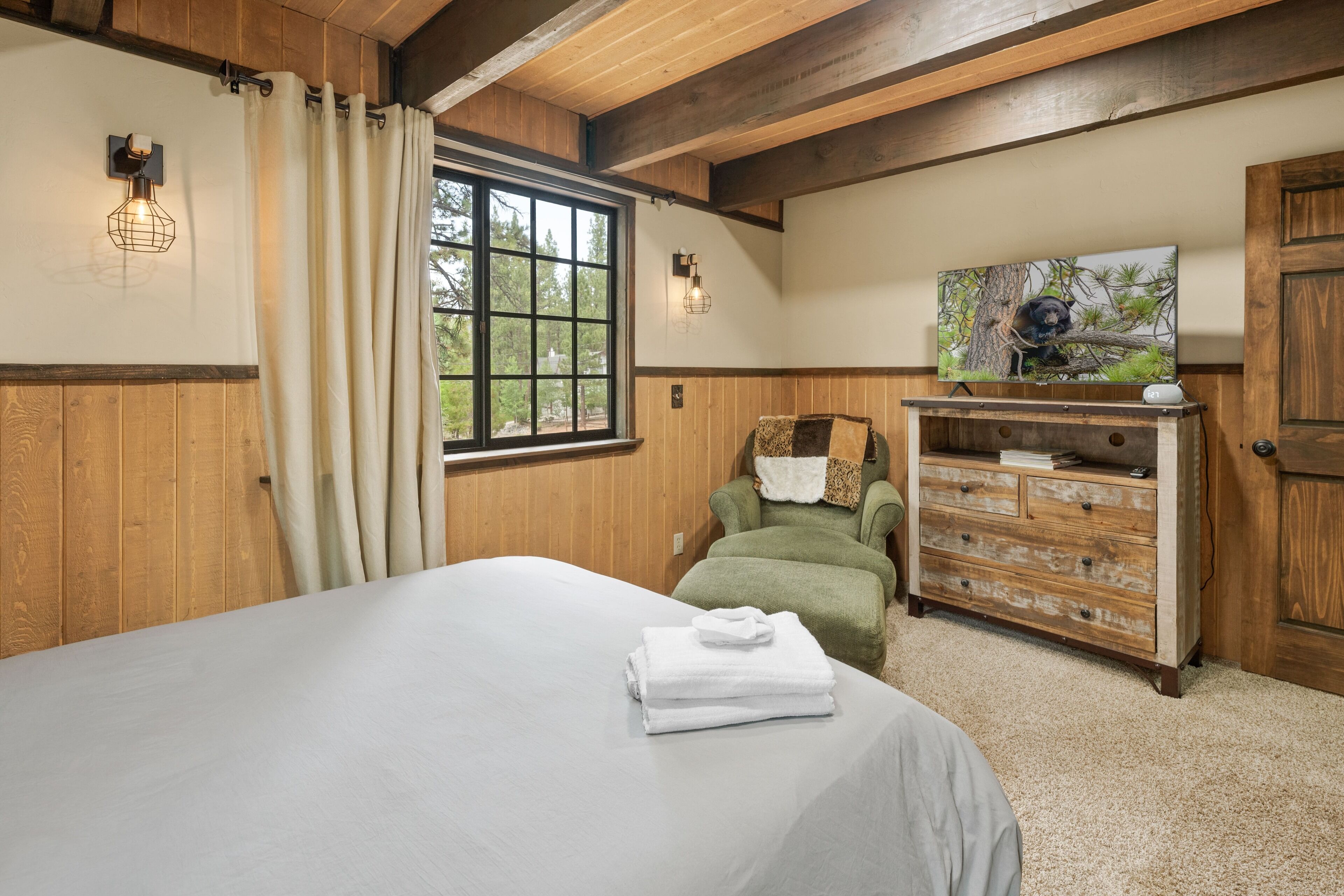 Quarto com uma cama grande, uma cadeira verde, cômoda de madeira e um quadro na parede.