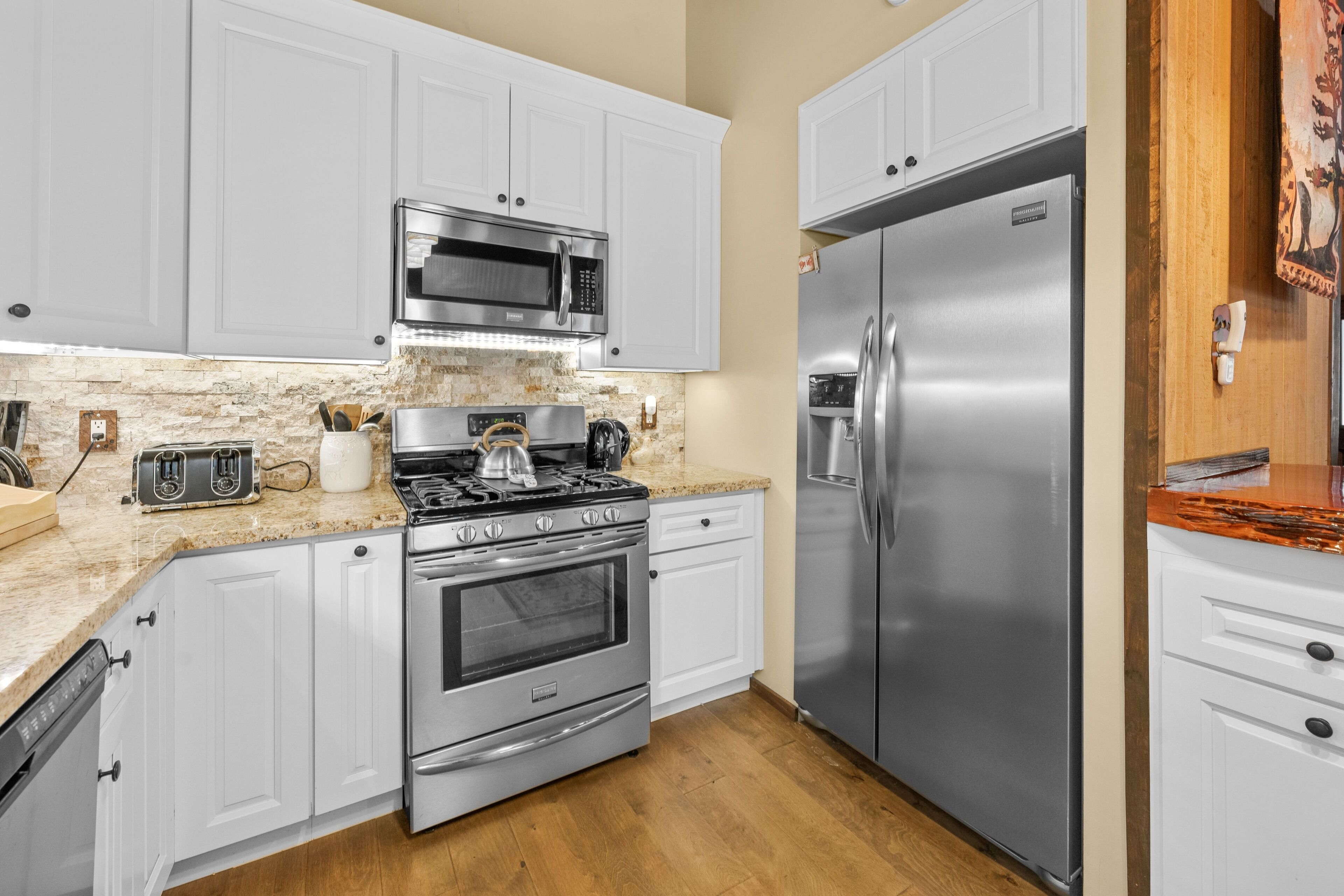 Una cocina moderna con gabinetes blancos, electrodomésticos de acero inoxidable, encimera de granito y un protector contra salpicaduras de madera.