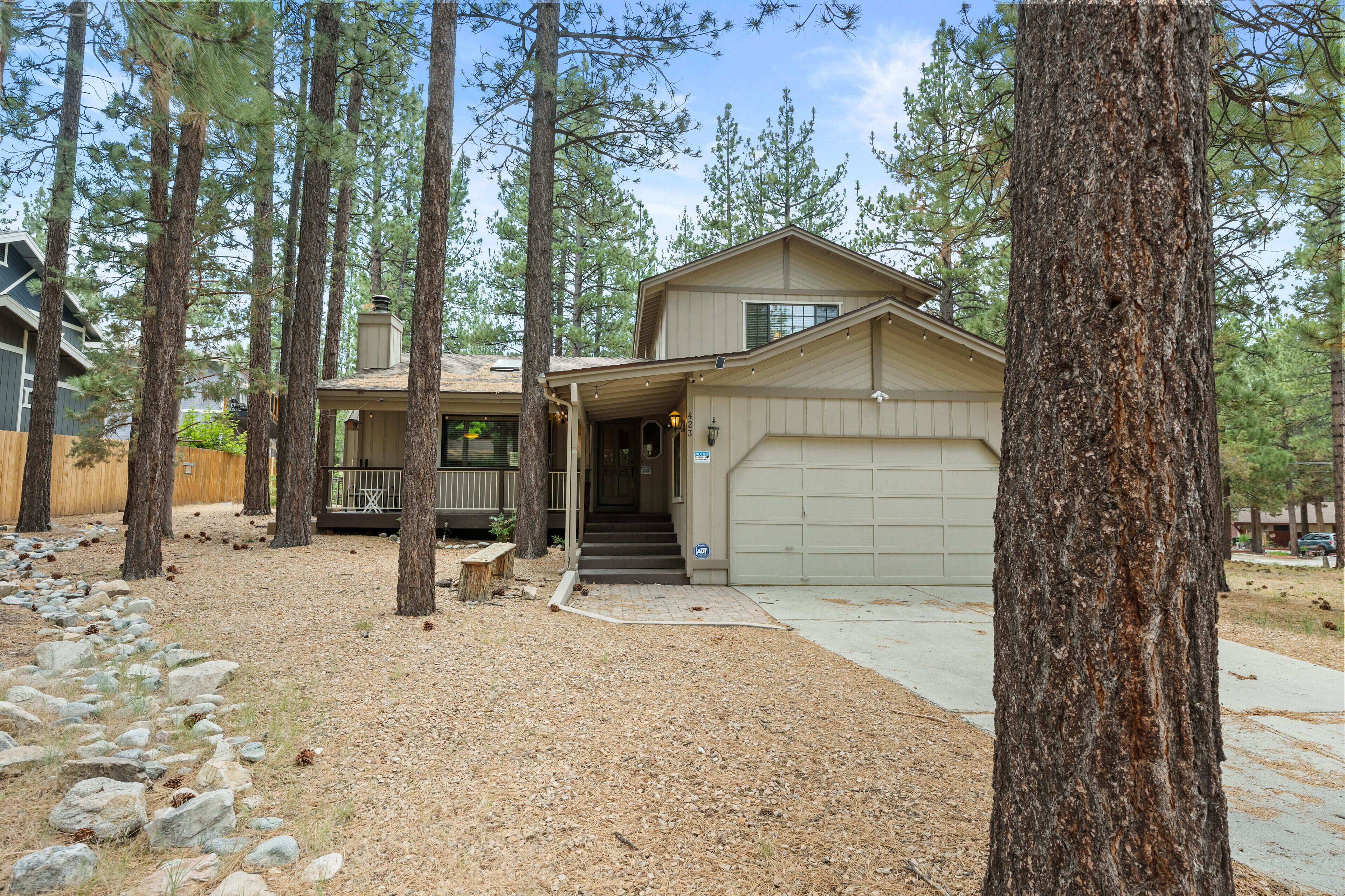 A two-story house with a garage, surrounded by tall pine trees.