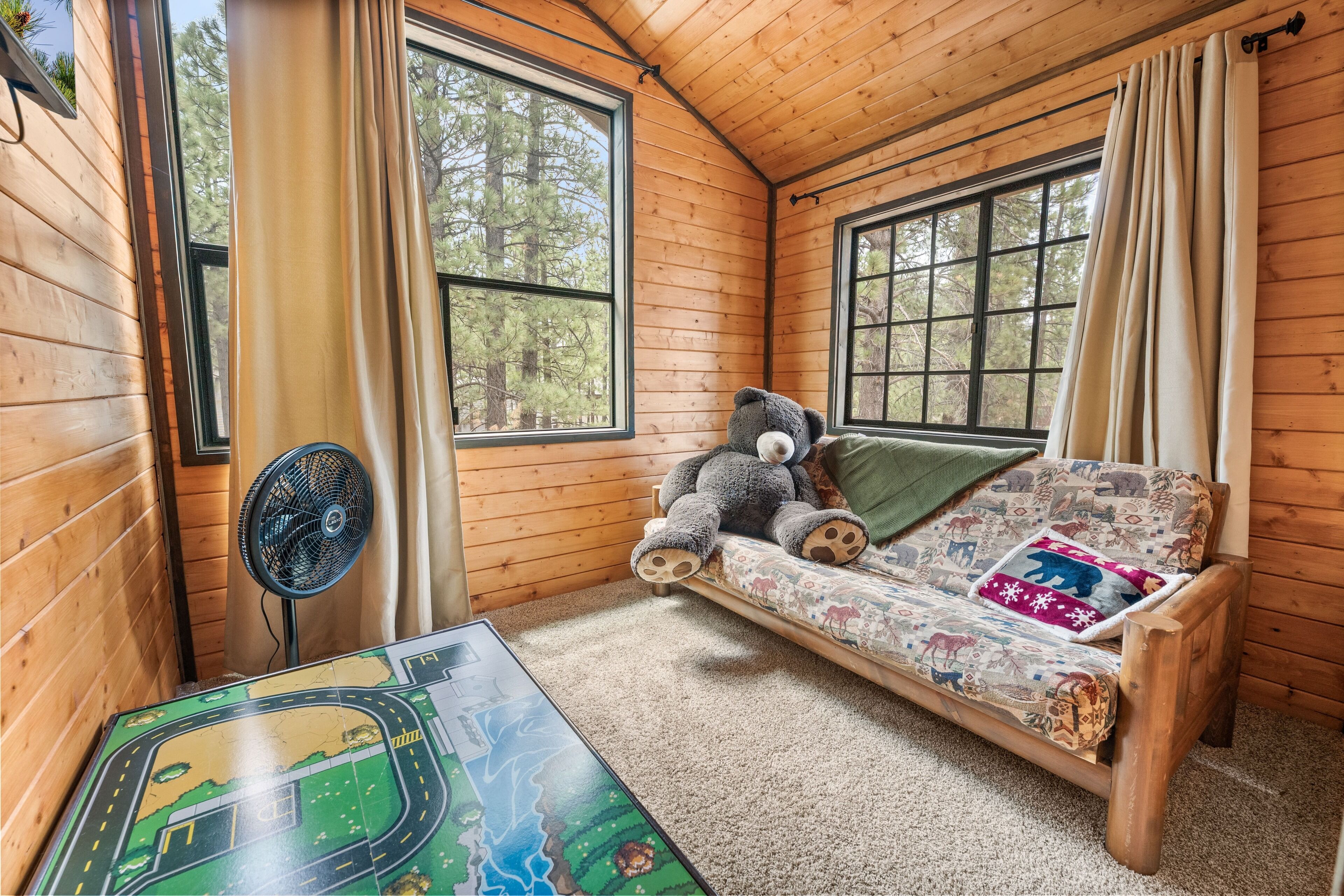 Ein gemütliches Cabin-Zimmer mit Holzvertäfelung, einem Schlafsofa mit Teddybär, einem Ventilator und einem Tisch für Brettspiele.