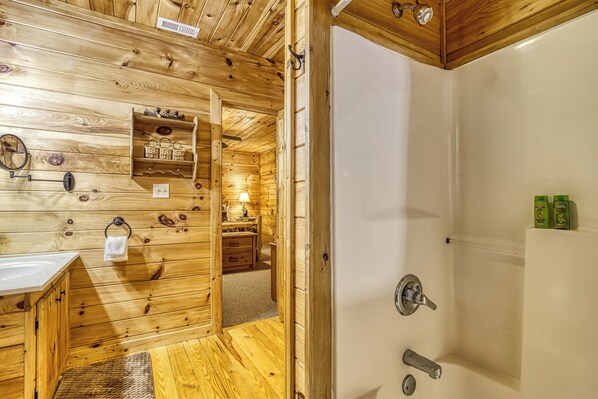 Interior de una cabaña de madera con baño que incluye ducha, lavamanos y tocador con espejo y perchero para toallas.