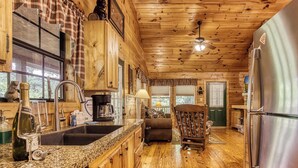 A wooden cabin interior with a kitchen featuring granite countertops, a refrigerator, and a dining area with a table and chairs. - Kozy Cub Cabin, Gated Resort, Pool Table (Sevier County)