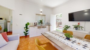 A modern living room with a sofa, a dining table with chairs, a kitchen area, and a TV mounted on the wall. - Quinta Casalinho - T2 Amendoeira (Guia)