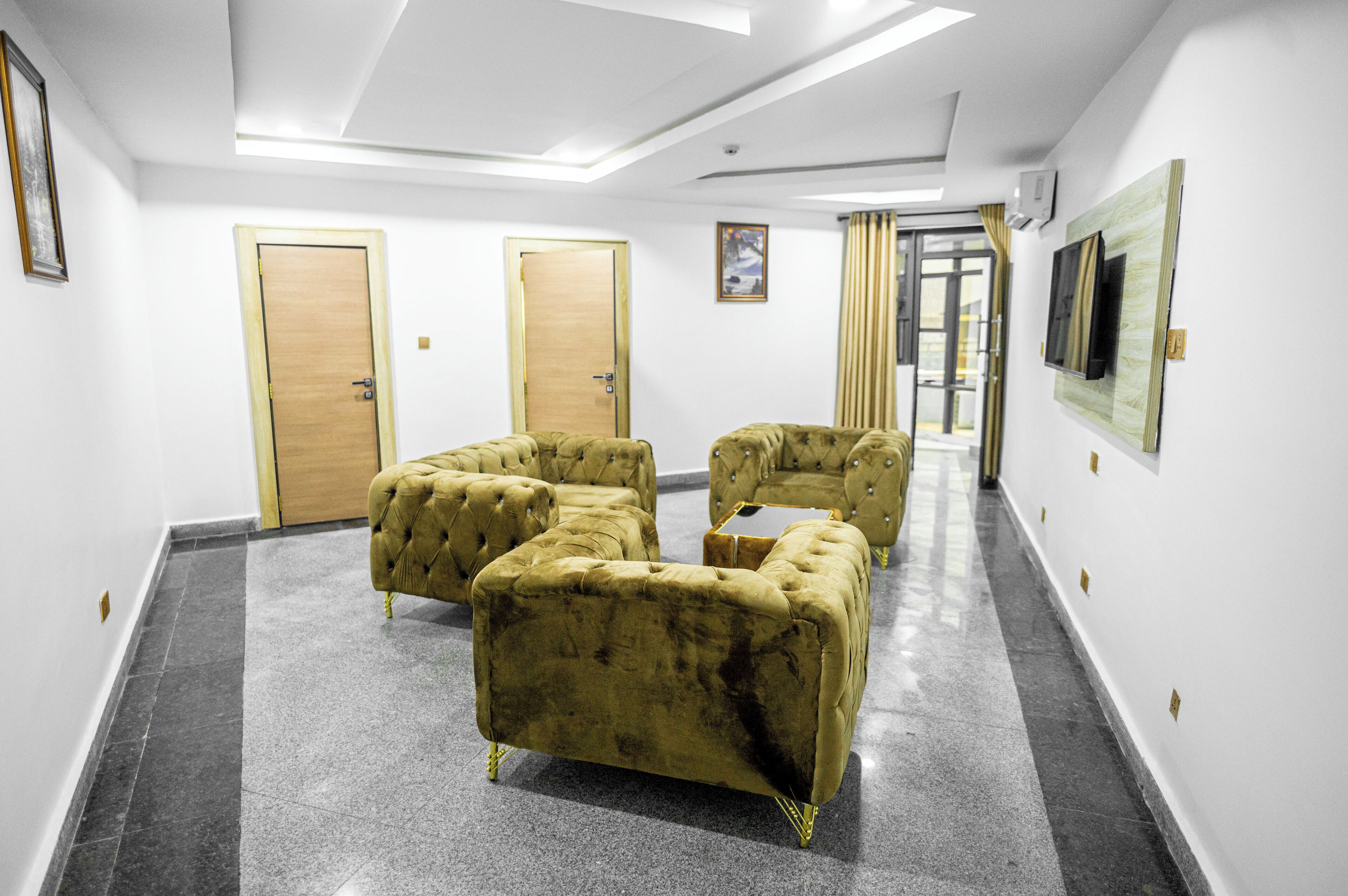 Une chambre d’hôtel au design moderne, comprenant un coin salon avec des canapés capitonnés, un téléviseur à écran plat fixé au mur et une grande fenêtre avec des rideaux.