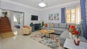 A living room with a sofa, coffee table, and a TV. There is a staircase leading to another room.