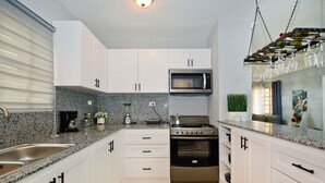 A modern kitchen with white cabinets, a stainless steel stove, a microwave, and a wine rack.
