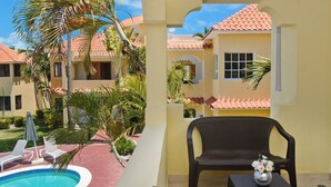 A pool area with lounge chairs, a table with a vase, and a view of a building with a tiled roof.