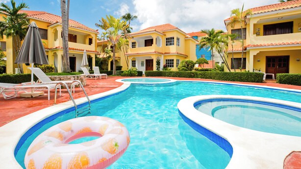 A swimming pool with two separate sections, surrounded by palm trees and lounge chairs.