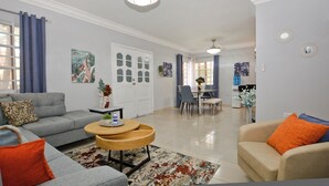 A living room with a grey sofa, beige armchair, and a wooden coffee table. There is a dining area with a table and chairs in the background.