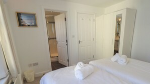 A hotel room with two beds, a large mirror, a door leading to a bathroom, and a small picture on the wall. - Swirl Howe (Keswick)