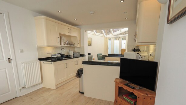 A modern kitchen with light wood cabinets, a black countertop, and a built-in TV. - Swirl Howe (Keswick)