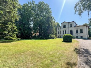 A large, multi-story building with a symmetrical facade, surrounded by a well-maintained lawn and dense trees.