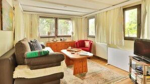 Una sala de estar con un sofá, un sillón rojo, una mesa de centro, un televisor y una estantería.