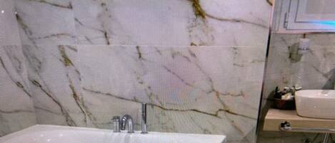 A bathroom with a marble wall, a bathtub, and a sink.