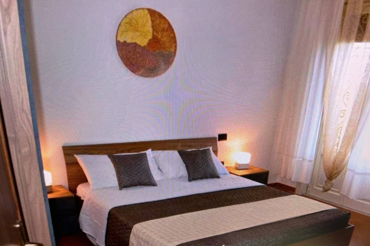 Een hotelkamer met een bed, nachtkastje, lamp en een kunstwerk aan de muur.