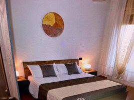 Una habitación de hotel con cama, mesita de noche, lámpara y una obra de arte en la pared.