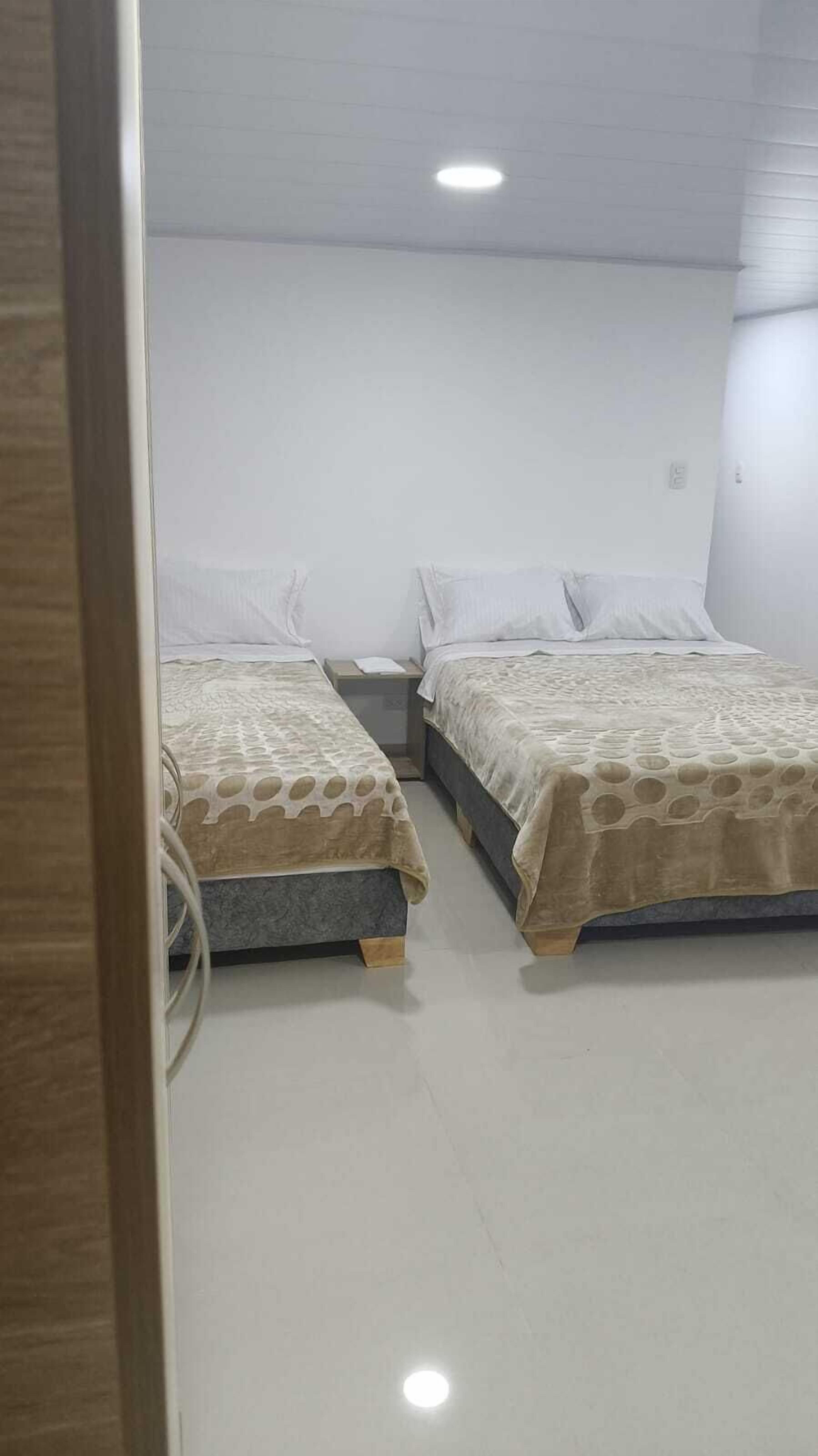 A small, clean room with two single beds, a nightstand, and a white wall.