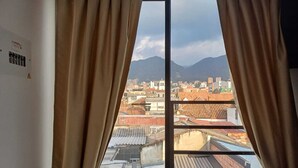 Finestra amb cortines beix, que mostra una vista de la ciutat amb edificis de teulada vermella i muntanyes a la distància.