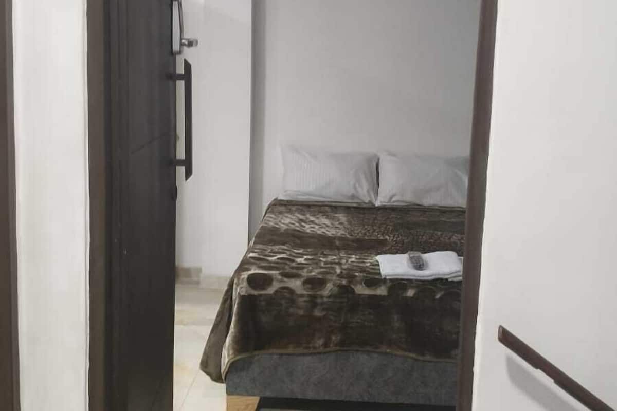 A narrow doorway leading to a bedroom with a bed, a nightstand, and a small table.