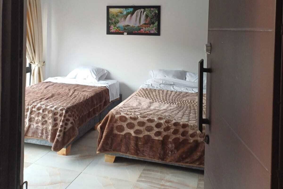 A hotel room with two beds, a painting of a waterfall on the wall, and a number 204 sign above the door.