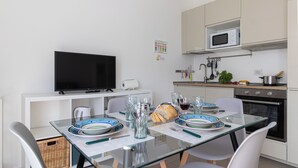 Una cocina moderna con una mesa de comedor para dos personas, un televisor de pantalla plana y un microondas sobre la encimera.