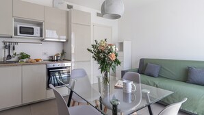 Cocina moderna con microondas, estufa y horno. Hay una mesa de comedor con sillas y un florero. Un sofá verde se encuentra en la sala.